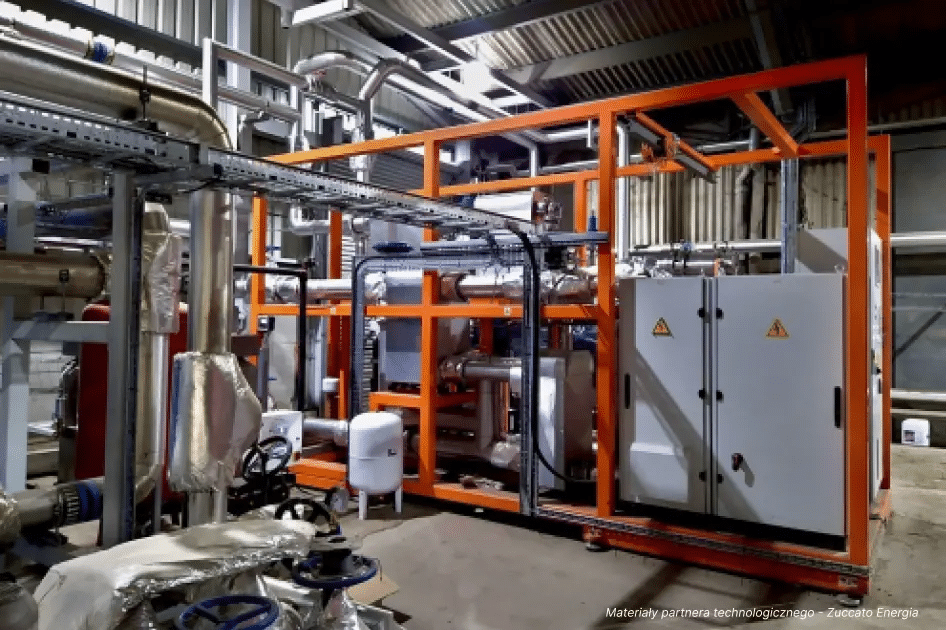 Industrielle Ausrüstung für die industrielle Energieversorgung mit orangefarbenen Metallrahmen, Schalttafeln, Rohren und isolierten Komponenten in einer sauberen, organisierten Fabrik. Warnschilder sind auf den Tafeln sichtbar.